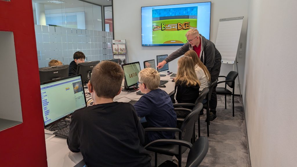 Dozent erklärt Schülern Programmieraufgaben am Computer in einem IT-Workshop